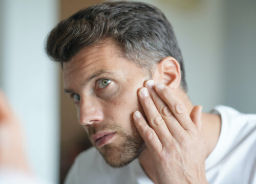 Photo of a man looking at his skin in the mirror