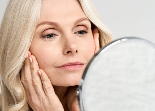 Photo of an older woman with great skin looking at her face in the mirror